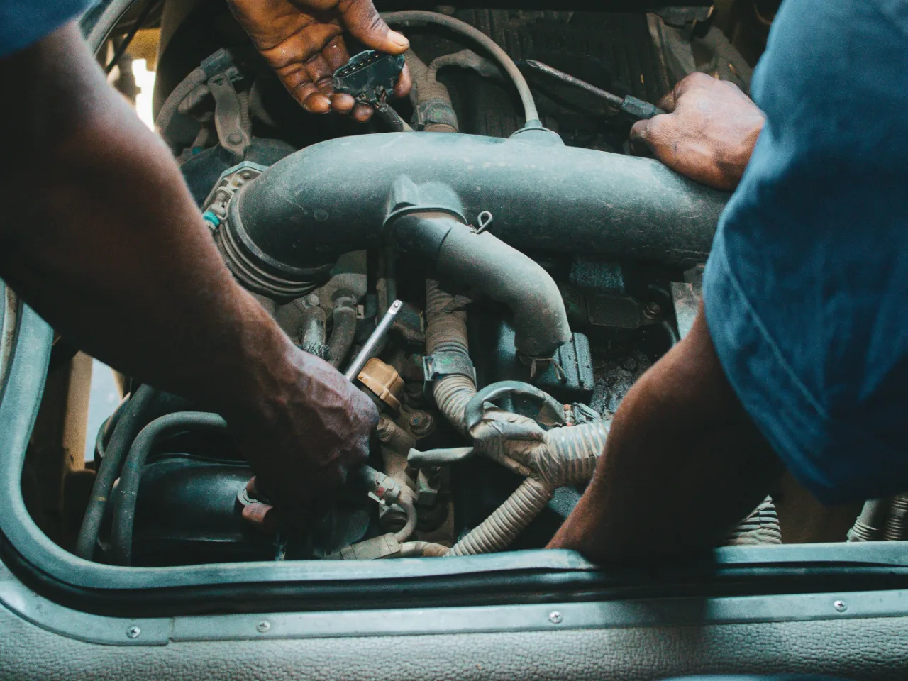 Deux paires de mains dans le compartiment moteur d'une voiture, capot ouvert.