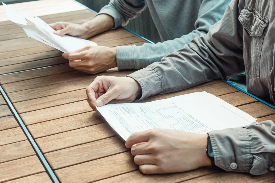 Deux paires de mains et deux documents sur une table de bois.