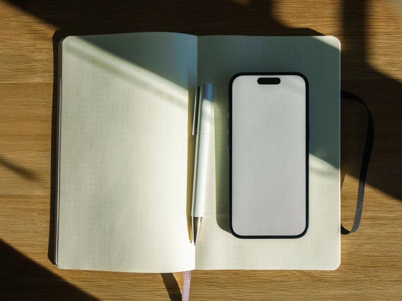 Un carnet ouvert, un stylo et un téléphone sur une table de bois, au soleil rasant.