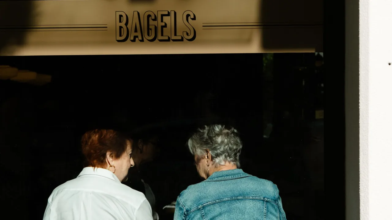 Deux clientes de dos, en pleine conversation au comptoir d'un commerce de quartier.