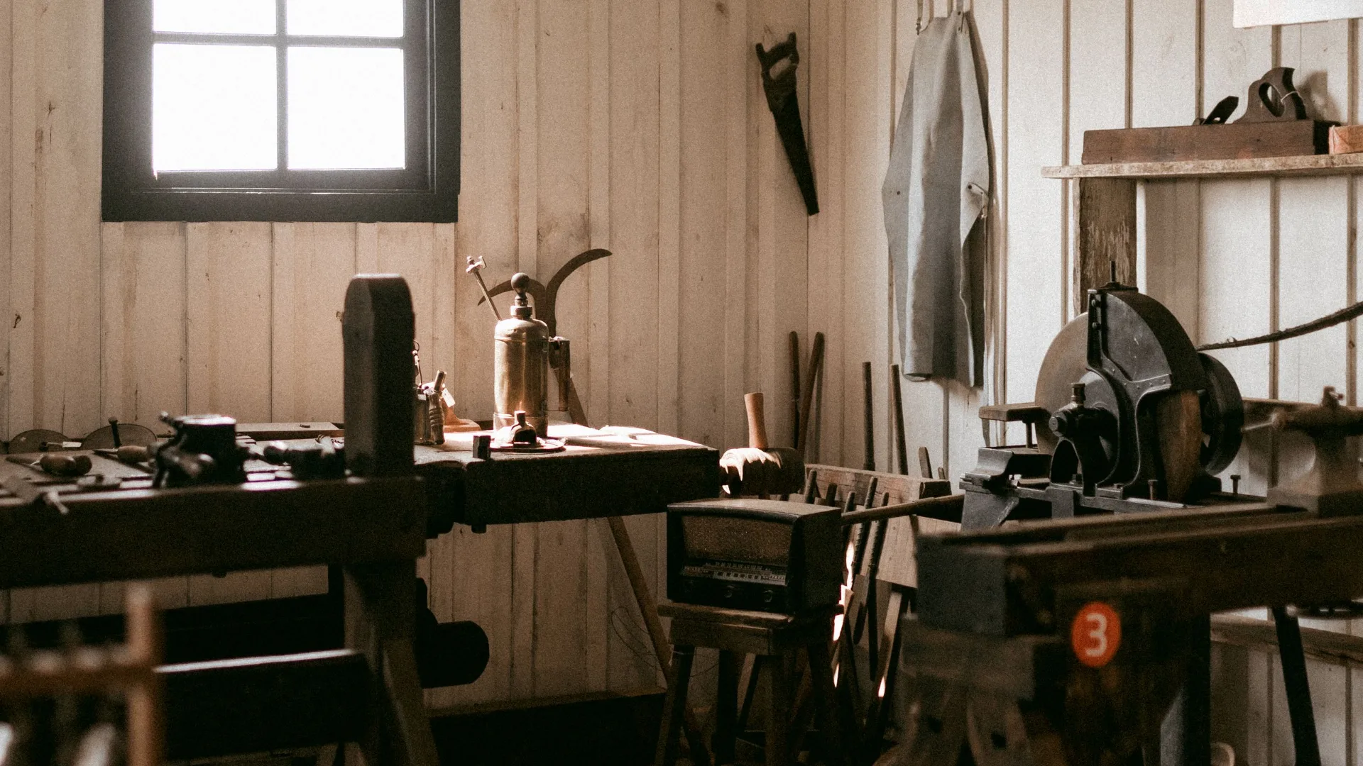 Un atelier de bois sous charpente : des établis, des servantes, de la lumière du jour, personne.