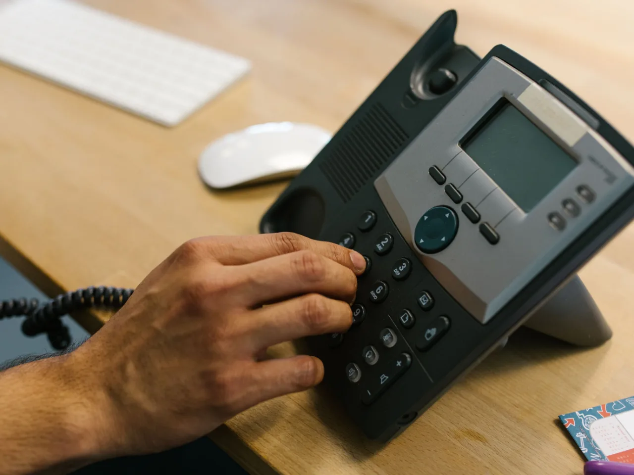 Une main compose un numéro sur un téléphone de bureau, dans une pièce claire.