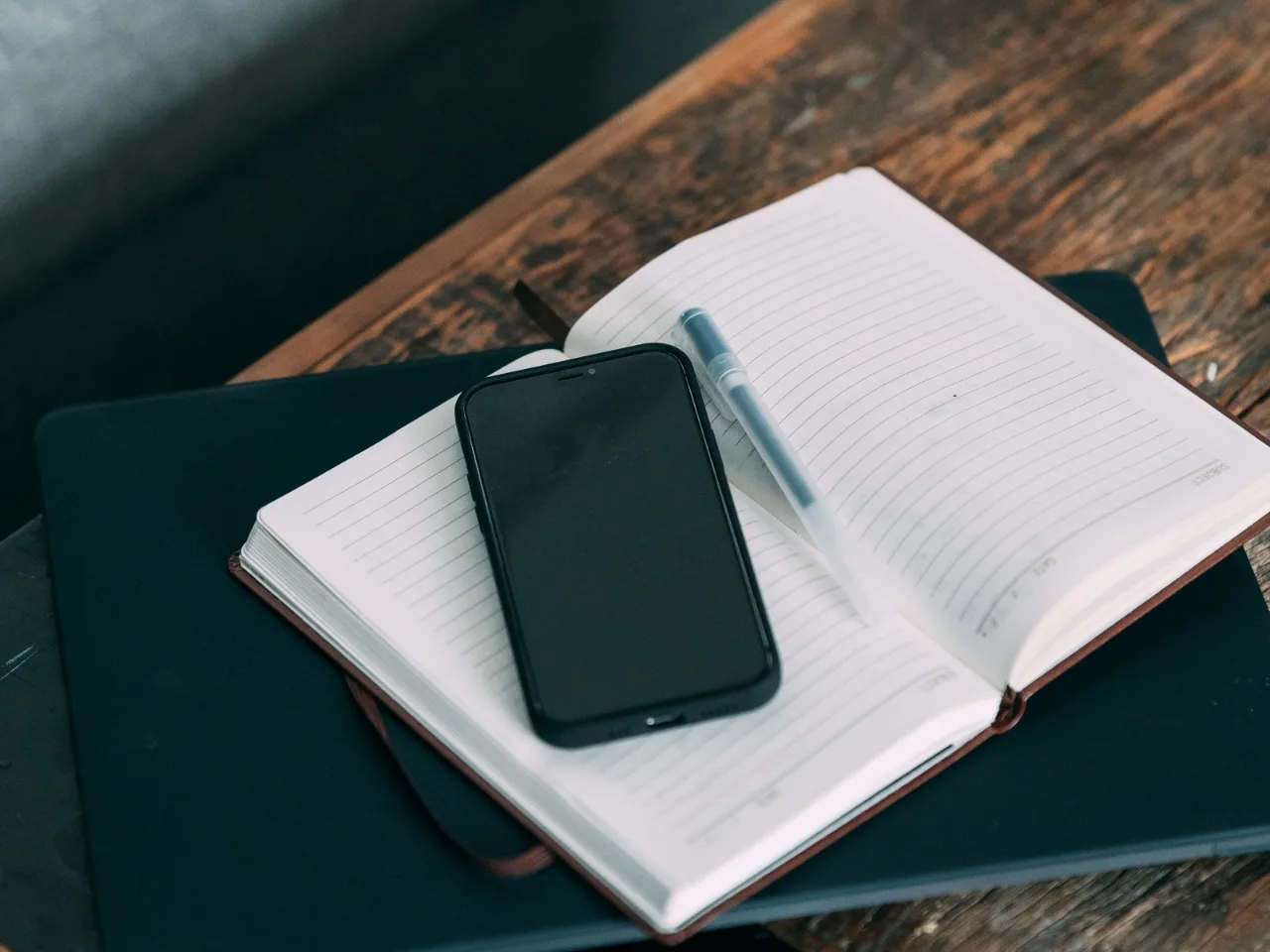 Un téléphone et un stylo posés sur un agenda ouvert, sur une table de bois sombre.