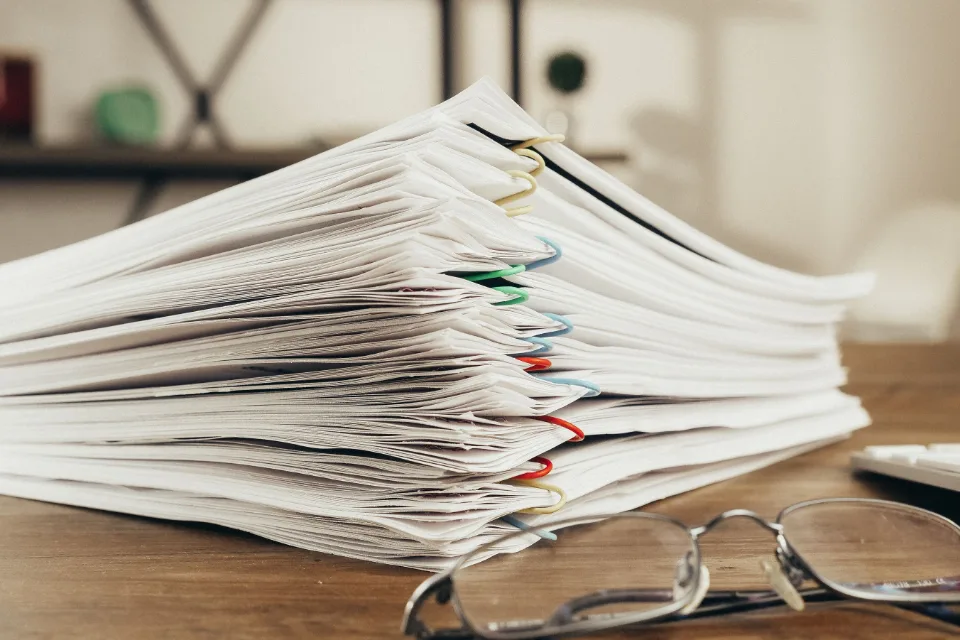 Une pile de formulaires remplis à la main, agrafés, et une paire de lunettes posée dessus.