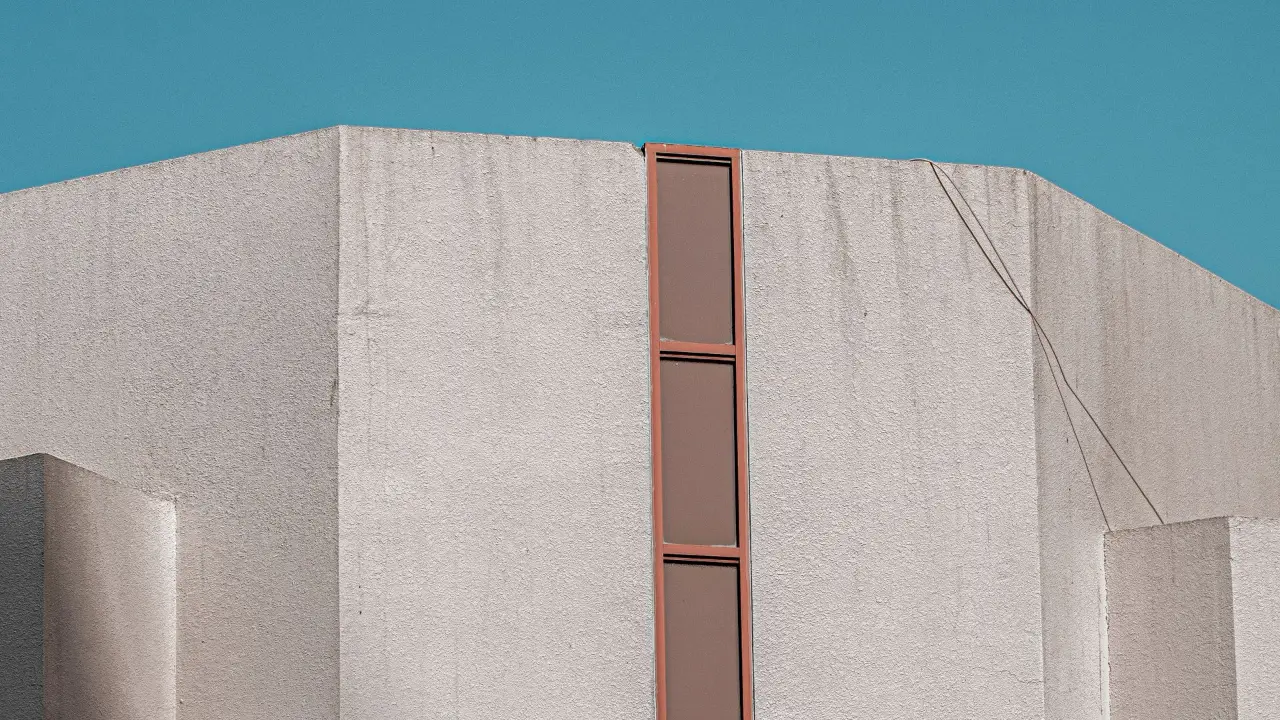 Un angle de béton clair coupé par une fente vitrée verticale, sous un ciel dégagé.