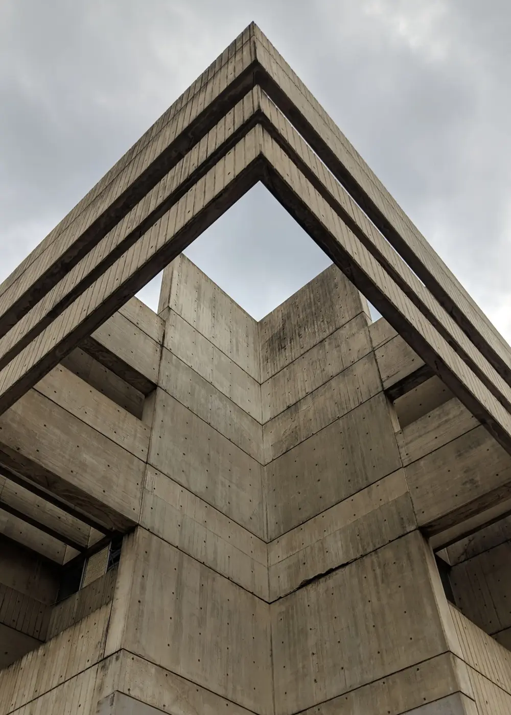 L'arête en chevron d'un volume de béton, vue en contre-plongée sur un ciel couvert.