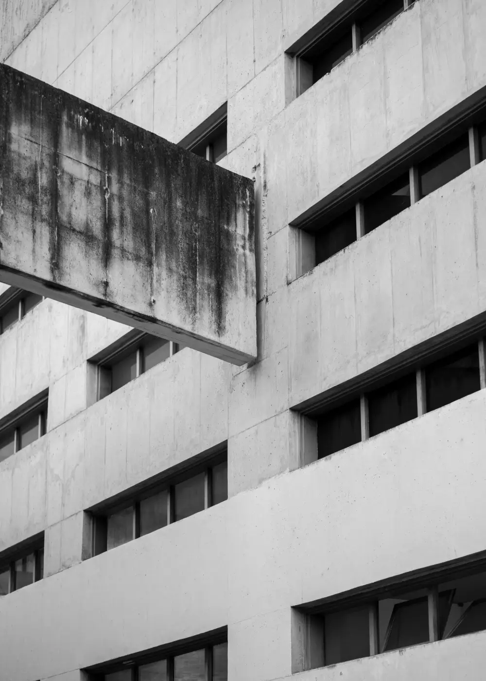 Une dalle de béton en porte-à-faux sort d'une façade percée de bandeaux de fenêtres.